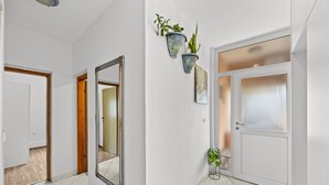 A hallway with white walls, a wooden door, a mirror, and two potted plants. - Charming three-bedroom apartment near the sea (Valbandon)