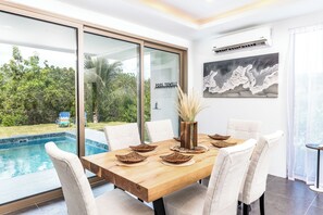 A dining area with a wooden table, white chairs, and a view of a swimming pool and greenery. - NEW Villa Golf Course views, Roof Top Hot Tub, near Grace Bay Beach- Gabriella 2 (Grace Bay)