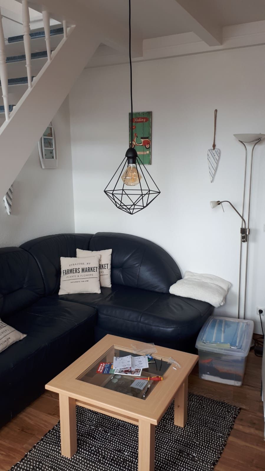 Una sala de estar moderna con un sofá de cuero negro, una mesa de centro de madera, un lámpara colgante y una lámpara de pie.