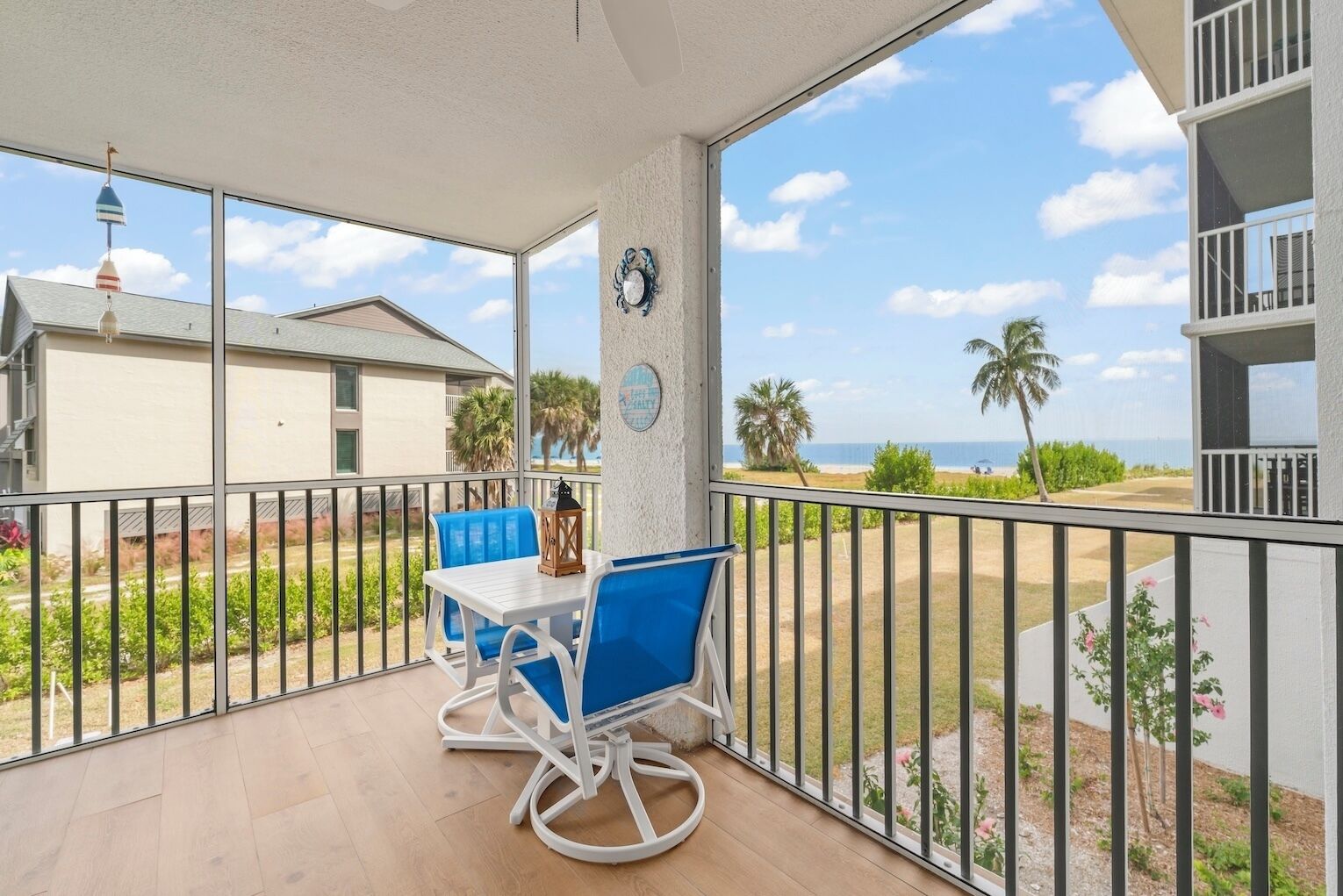 A balcony with a table and chairs, a clock, and a view of the beach and ocean.