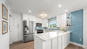 Une cuisine moderne avec des meubles blancs, des appareils en acier inoxydable et un pare-feu bleu.