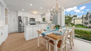 Une cuisine moderne avec des meubles blancs, des appareils en acier inoxydable et un coin repas comprenant une table en bois et des chaises blanches.