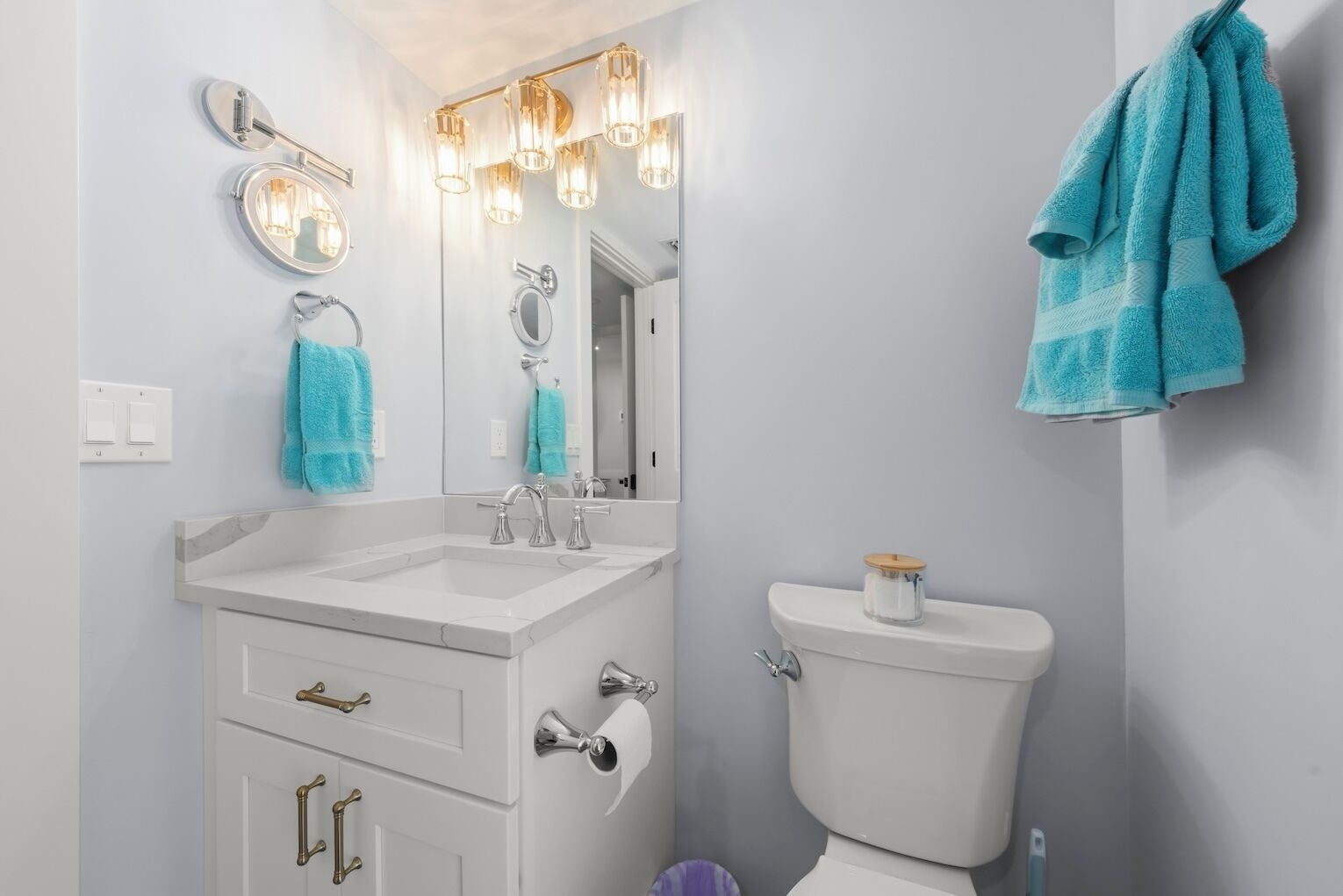 Et badeværelse med et hvidt toiletbord, toilet og et spejl med lys.