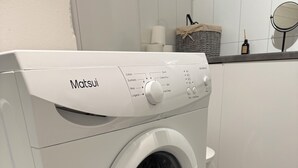 Una lavadora de carga frontal blanca Matsui en una cocina con piso de baldosas oscuras.