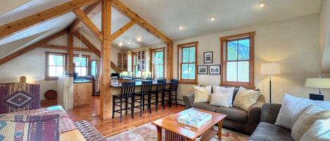 A spacious loft-style living area with a high ceiling, wooden beams, a kitchen with bar stools, a sofa, and a coffee table.