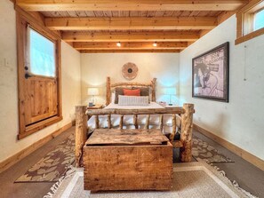 A rustic bedroom with a wooden bed frame, a nightstand, a bedside table, a decorative wall piece, and a large wooden chest. - 312 First Street — 3-Bedroom Home in the Heart of Crested Butte (Crested Butte)