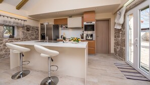 A modern kitchen with a central island, bar stools, a stone wall, and a large window. - Villa Didova ku a Zadarvillas (Benkovac)