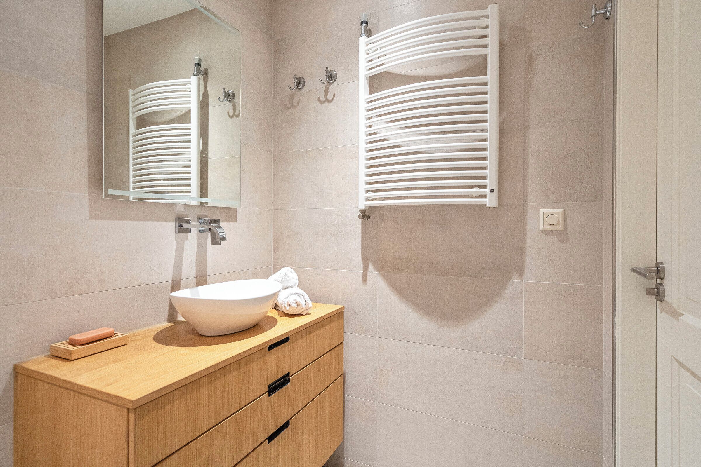 Ein modernes Badezimmer mit Waschtisch aus Holz, einem großen Spiegel und einem weißen Handtuchhalter.