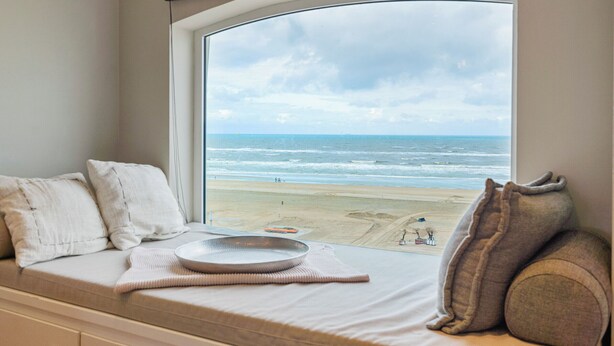 A view from a window with a beach scene, a cushioned bench, and a tray with a bowl. - Sandhues Beachfront Apartment (Zandvoort)