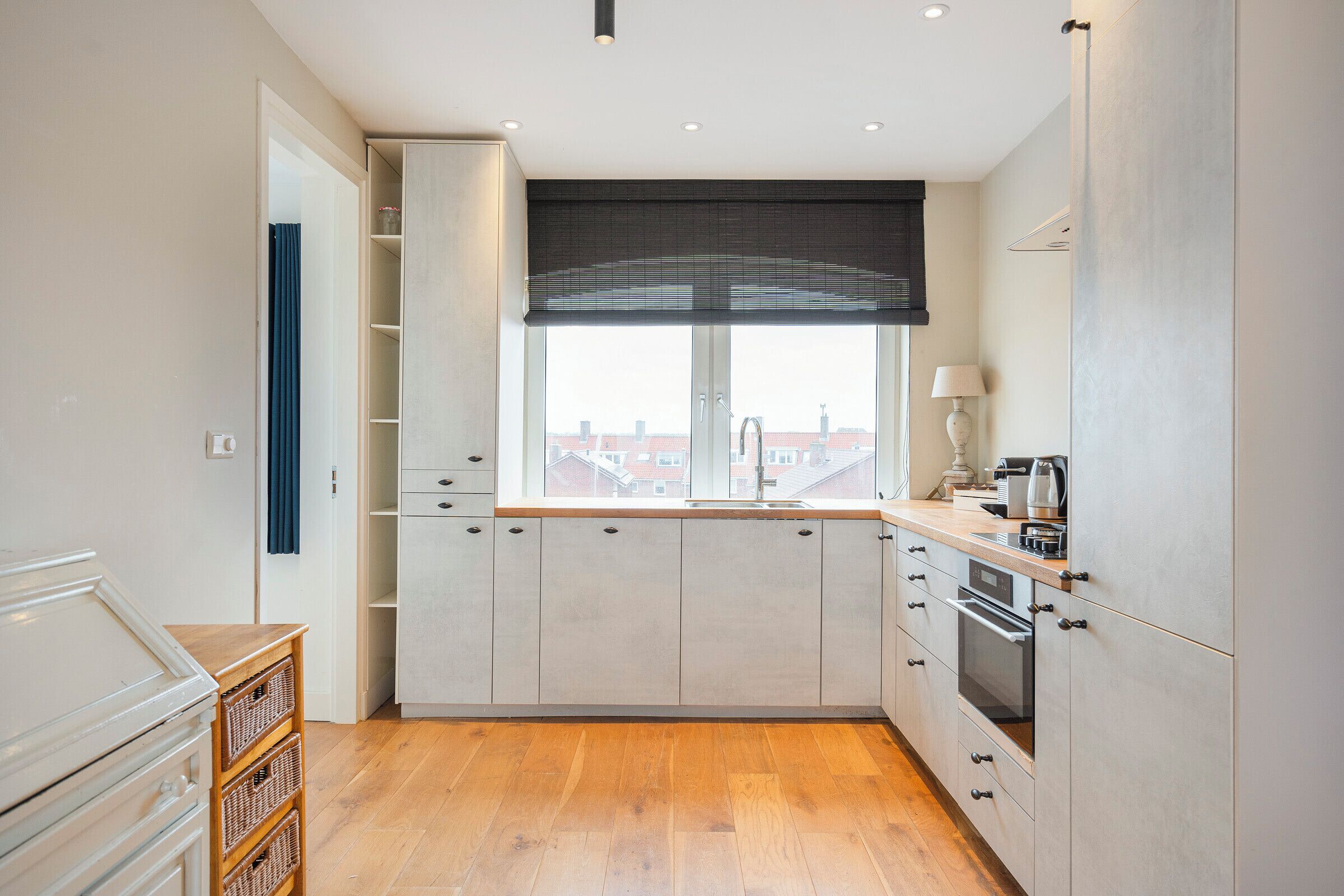 A modern kitchen with a large window, built-in cabinets, and a wooden floor.