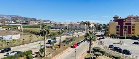 A parking lot with multiple cars, palm trees, and a building with a red and yellow facade.