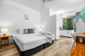Ein modernes Schlafzimmer mit einem großen Bett, Nachttischlampen, einem kleinen Tisch und Blick zur Küche durch eine offene Tür.