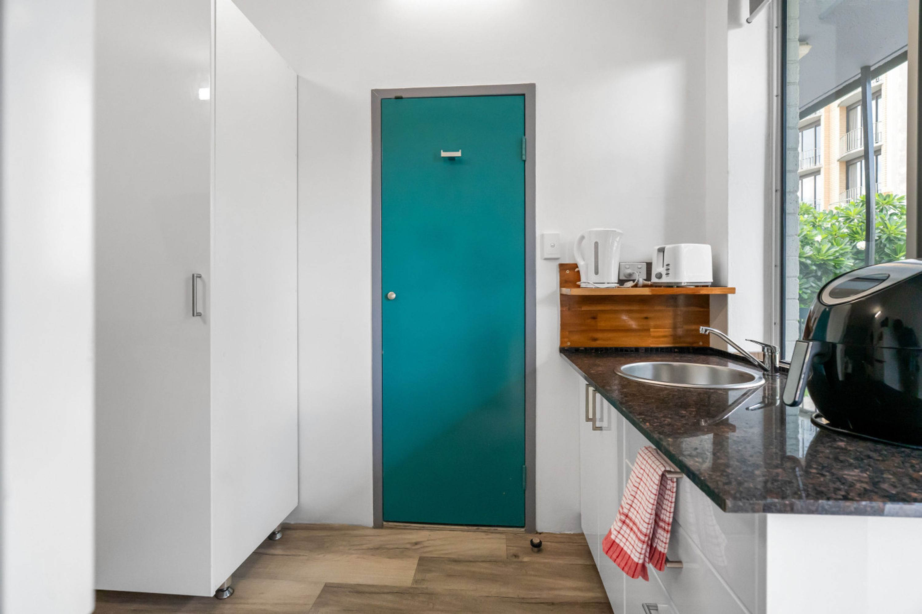A compact kitchen with a teal door, a sink, a coffee maker, and a toaster on a countertop.