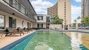 Una piscina con sillas de descanso, un edificio con un mural de delfines y un rascacielos al fondo.