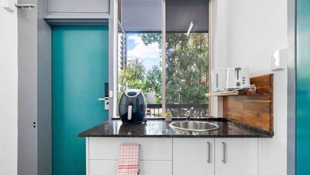 Una cocina moderna con encimera negra, armarios blancos, pared de acento verde azulado y ventana con vistas a la vegetación.