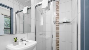 Un baño moderno con lavamanos blanco, espejo y cabina de ducha de vidrio.