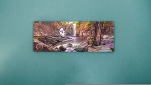 Fotografía enmarco de una cascada con una persona de pie junto al agua, rodeada de rocas y árboles.
