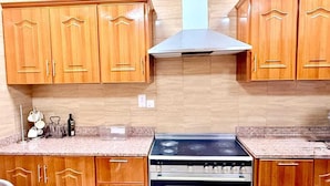 A kitchen with wooden cabinets, a stainless steel range hood, and a double oven. - Rizq Luxurious Villa (Dubai)