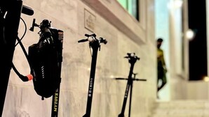 A row of electric scooters lined up against a wall with a person walking in the background. - Rizq Luxurious Villa (Dubai)