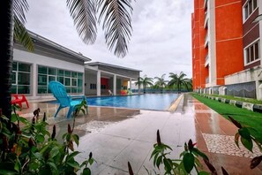A swimming pool area with a blue chair, a red chair, and a building with large windows. - Pavilionvillie M1T584 by Irainbow (Kinta)