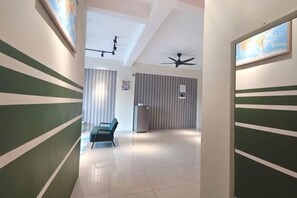 Un pasillo con paredes a rayas, un ventilador de techo, una lámpara en el techo, una silla y un refrigerador.
