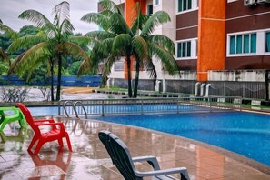 Una piscina con sillas, palmeras y un edificio con ventanas y barandilla.