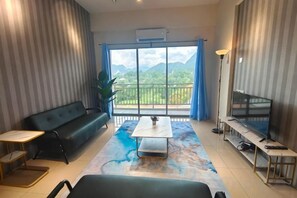 Una sala de estar moderna con un sofá, una mesa de centro y un televisor, con un amplio ventanal que ofrece vistas a montañas.
