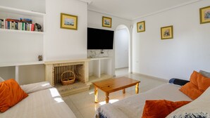 Una sala de estar con chimenea, televisión y sofá con cojines naranja.