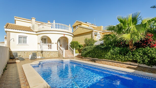 Vista de la piscina de una villa de estilo mediterráneo, con una alberca, un porche cubierto y una escalera que conduce a la entrada.