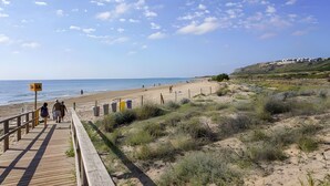 Una pasarela de madera que conduce a una playa, con cielo despejado y edificios a lo lejos.