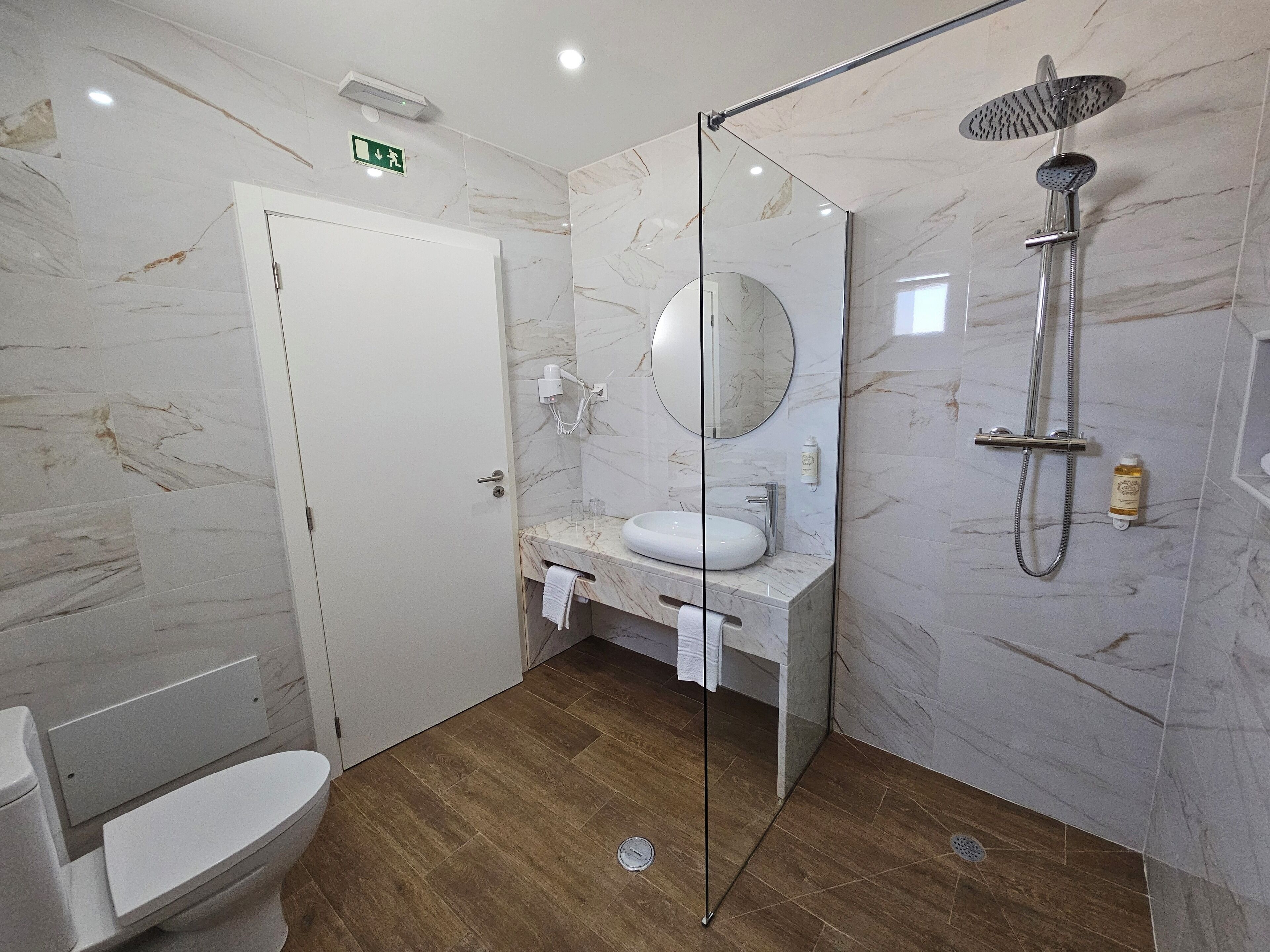 Un baño moderno con ducha envuelta en vidrio, un lavabo blanco y pared revestida de mármol.