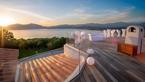 Eine Terrasse mit weitem Panoramablick auf einen See und Berge, mit Holzboden und weißer Gartenmöbeln.