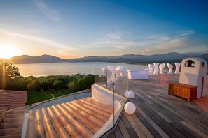 Eine Terrasse mit weitem Panoramablick auf einen See und Berge, mit Holzboden und weißer Gartenmöbeln.