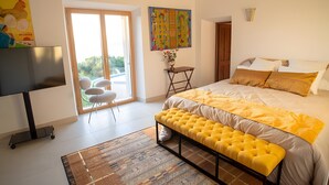 Ein Schlafzimmer mit einem Bett, einer Sitzbank, einem Fernseher, einer Tür und einem Fenster.