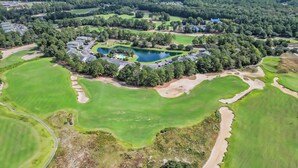An aerial view of a golf course with a central pond, surrounded by trees and buildings. - TB 37C Spacious 3-Bed, 2-Bath Second-Floor Condo in True Blue Community (Pawleys Island)