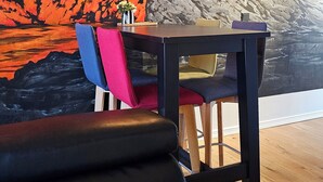 Un espace repas agrémenté d’une fresque représentant une éruption volcanique, de chaises en bois et d’une table.