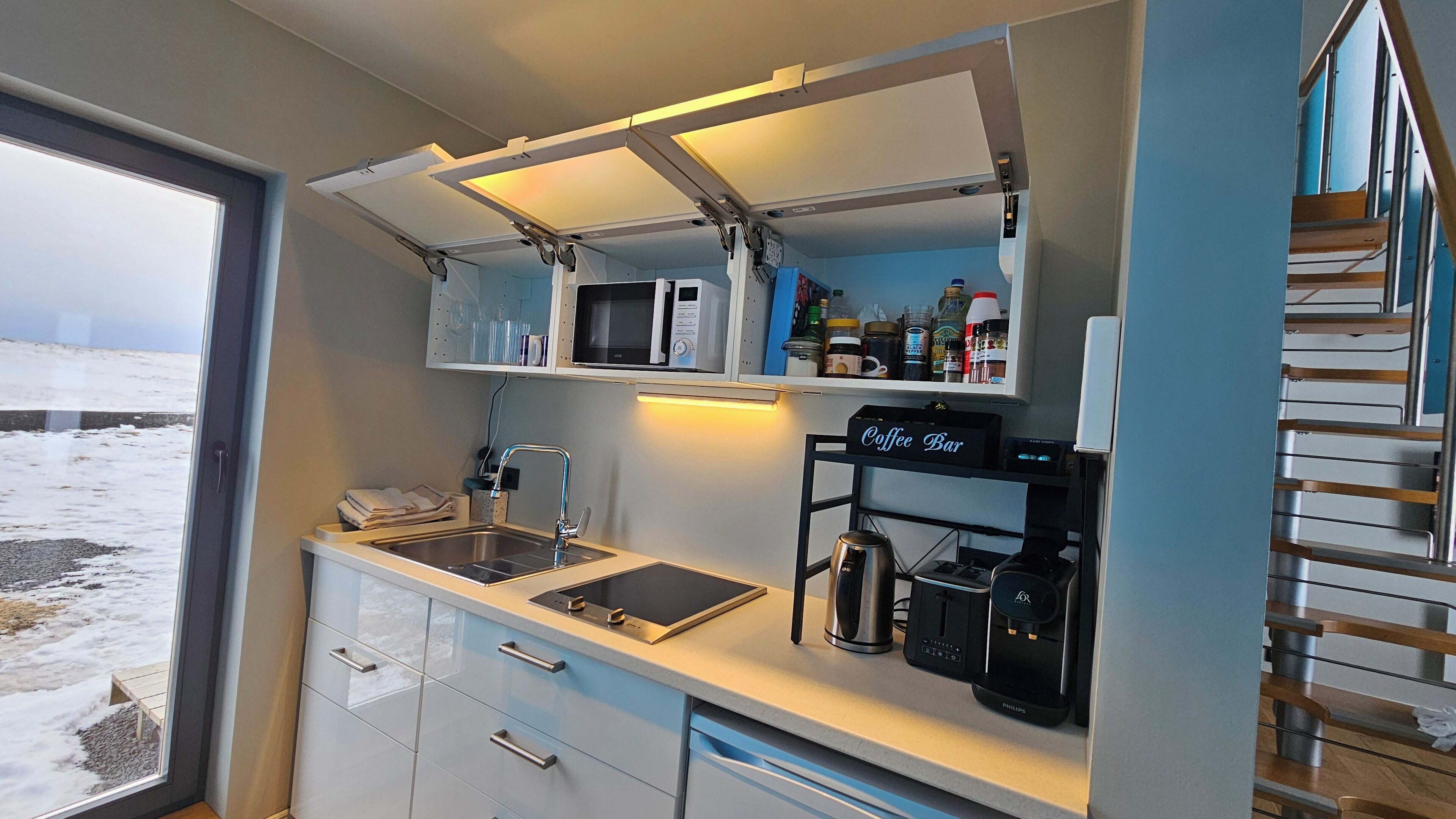 Cocina compacta con lavamanos, microondas, cafetera y refrigerador pequeño.