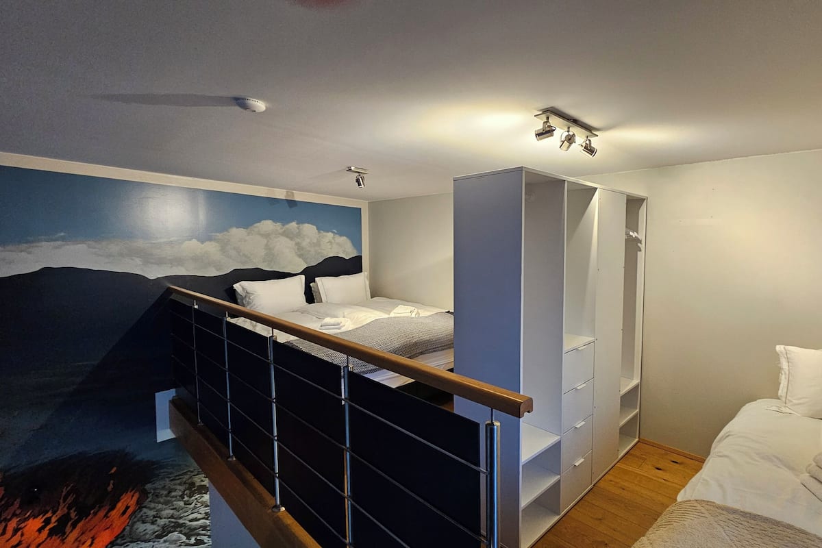 A bedroom with a bed, a wardrobe, a ceiling-mounted projector, and a wall mural of clouds.