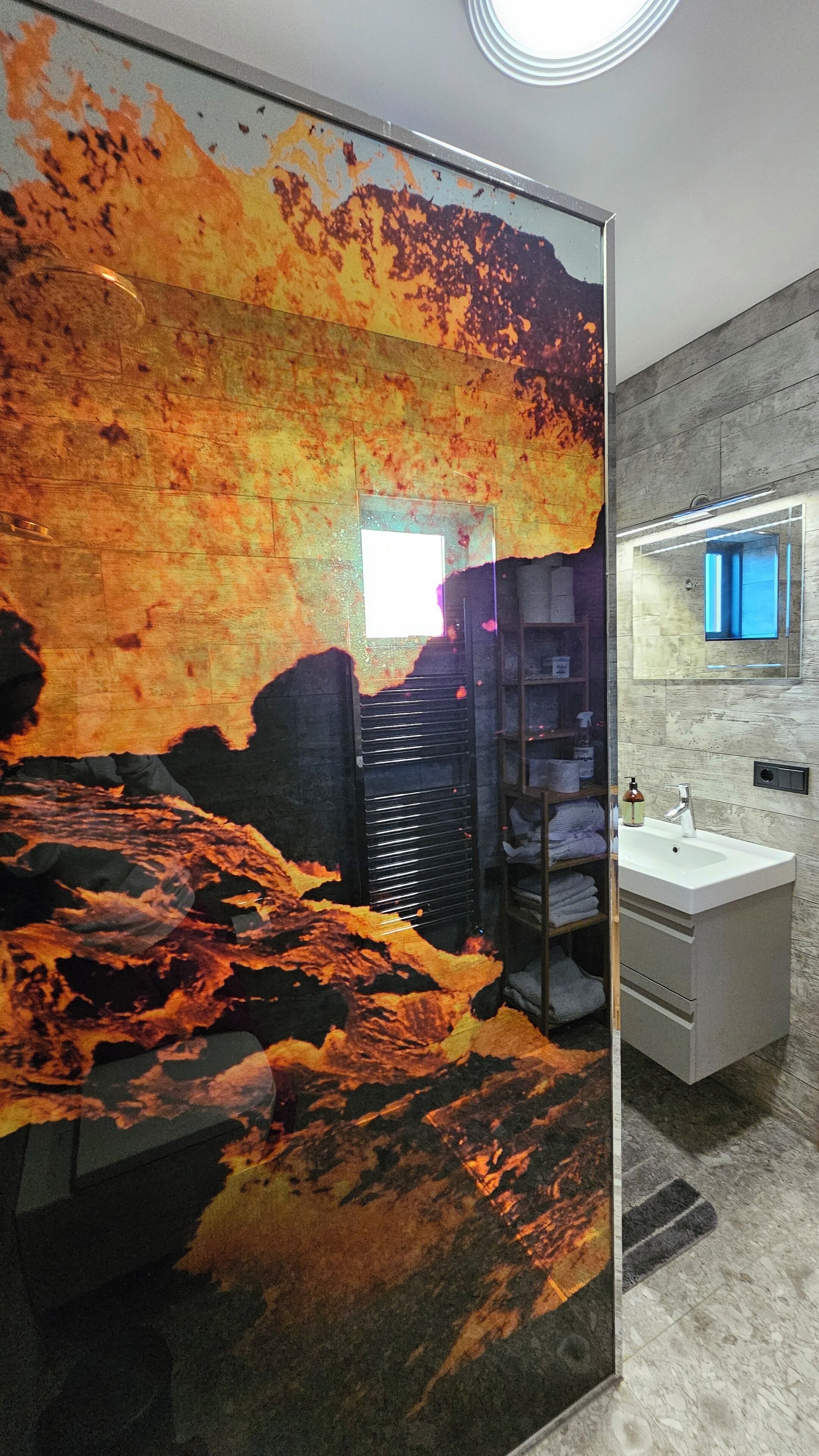 Ein Badezimmer mit Wandmalerei, die einen Lavastrom darstellt, sowie ein Waschbecken und ein Spiegel.