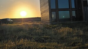 Un bâtiment moderne doté d’un toit plat et de grandes fenêtres, situé dans un champ verdoyant, avec une voiture garée à proximité.