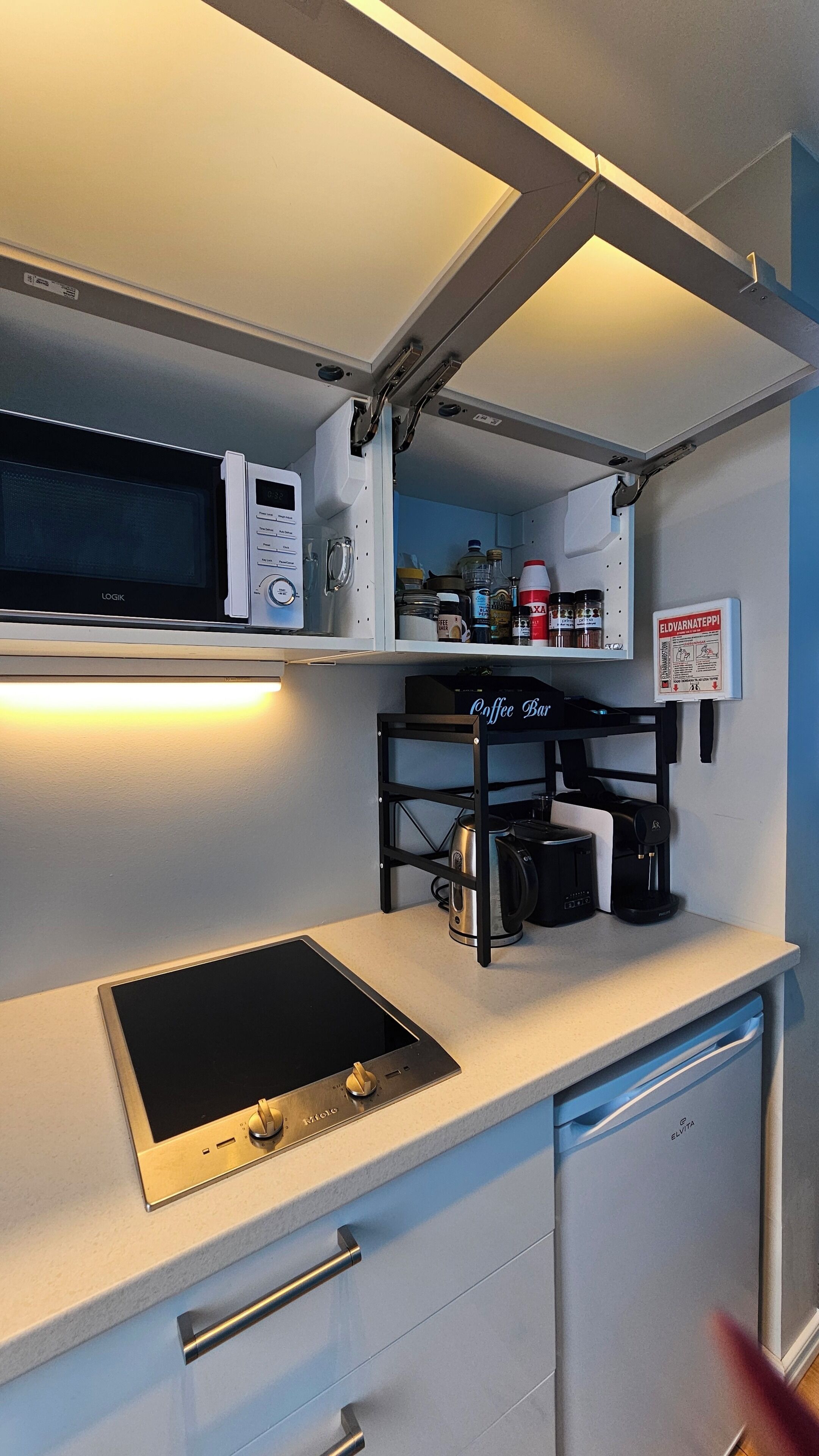 Una kitchenette funcional con microondas, cafetera y alacenas.