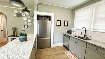 A kitchen with a stainless steel refrigerator, granite countertops, and a patterned rug.