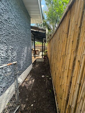 A narrow outdoor space with a covered patio area, a bamboo fence, and a dark textured wall. - The Duchess:Vintage Revived-Pets Welcome (Jacksonville)