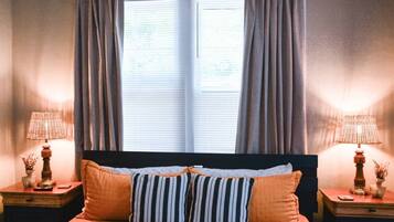 A bedroom with a bed, two nightstands, a window with curtains, and two lamps.