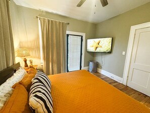 A bedroom with a bed, a television, a window with curtains, and a door. - The Duchess:Vintage Revived-Pets Welcome (Jacksonville)
