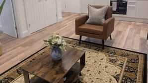 Una sala de estar moderna con un sofá de cuero marrón, una mesa de centro de madera con un jarrón de flores y una alfombra estampada.