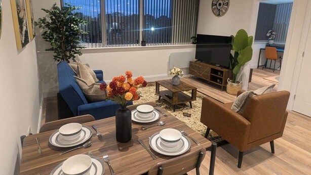 Una sala de estar moderna con comedor, un sofá, un televisor y un amplio ventanal con persianas.