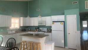 Uma cozinha com armários brancos, uma ilha central com bancos, micro-ondas, fogão e geladeira.