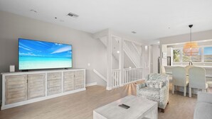 A modern living room with a large flat-screen TV, wooden flooring, and a staircase leading to an upper level. - Completely Updated 2BR Condo–Cedars East #613 by RVA (Longboat Key)
