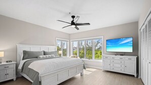 A bedroom with a bed, nightstands, a dresser, a TV, and a ceiling fan. - Completely Updated 2BR Condo–Cedars East #613 by RVA (Longboat Key)